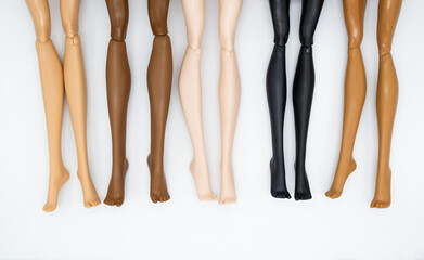 Legs of dolls representing different races on a white background. The concept of female friendship,...