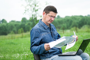 Businessman sitting at the office desk work at laptop computer in green forest park. Freelancer with hands on chin working on office table in green park. Business portrait.