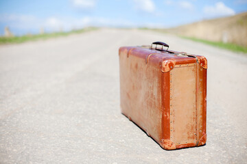 Old brown suitcase stands on desert road