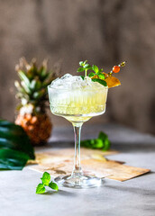 Cold freshly squeezed pineapple juice with crushed ice and mint on a light gray concrete background.