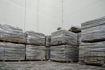 stacks of paving slabs on wooden pallets with transparent foil stored at light wall