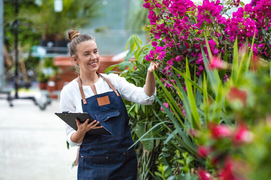 Young woman taking notes while working in a greenhouse. Woman working in a garden center and taking notes of her plants. Portrait of a young woman at work in greenhouse