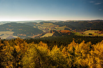 Sunset over autumn forest, fields and meadow in backlight. Evening sunbeams on meadow. Warm sun light in countryside of Bohemian Moravina Highlands, Žďár Hills, Vysocina, Czech Republic.