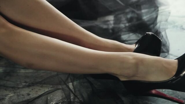 Slim female legs on the floor in black shiny high heel shoes