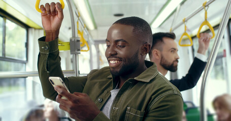 Portrait of young smiling african american man using smartphone in bus. Handsome male with cell...