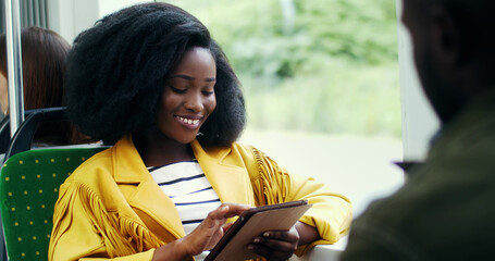 Portrait of smiling african american girl with an afro hairstyle using tablet in public transport.