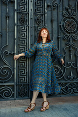 Beautiful attractive confident adult middle aged woman in blue dress posing against metal decorative gates outdoors