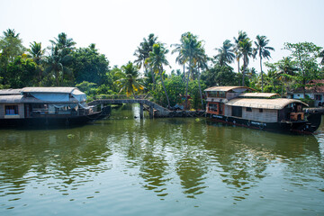 Small houses in a local village located next to Kerala's backwater on a bright sunny day and traditional Houseboat seen sailing through the picturesque backwaters of Allapuzza or Alleppey in Kerala 