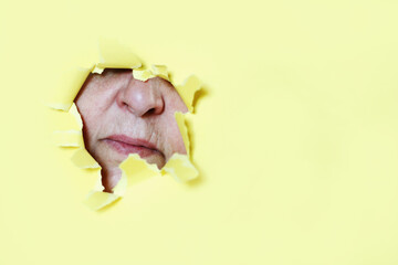 A woman looks through a hole in yellow paper wall 