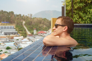 Gandsome man in black sunglasses spends time standing in swimming pool copyspace. travel concept