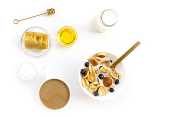 Fototapeta na wymiar Mini Pancake cereal pancakes with honey and honeycomb, yogurt, milk and blueberry on white plate and coffee on white cup. Isolated on white