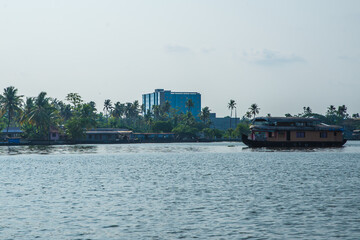 Small houses in a local village located next to Kerala's backwater on a bright sunny day and traditional Houseboat seen sailing through the picturesque backwaters of Allapuzza or Alleppey in Kerala 