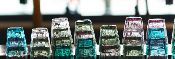 Many colorful backlit bar glasses stacked in a row on the counter of a restaurant.