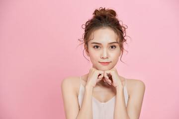 Pretty girl looking at camera and smiling, holding hands near face over pink background.