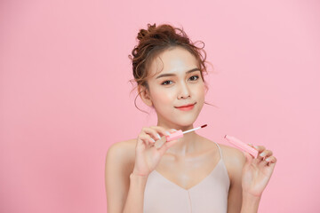 Young smiling Asian girl applying lipstick isolated over pink background.
