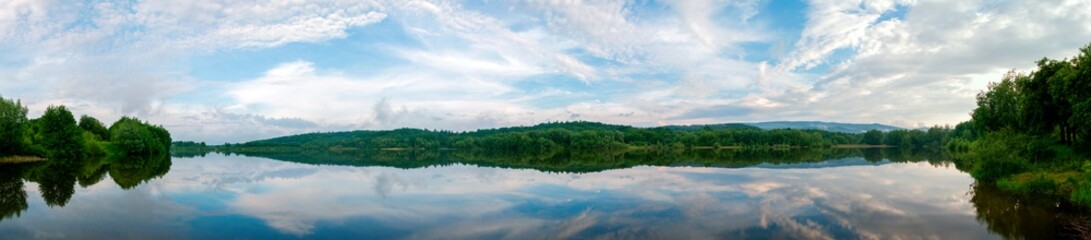 Panoramic landscape from the lake shore with colorful clouds in the spring sun.