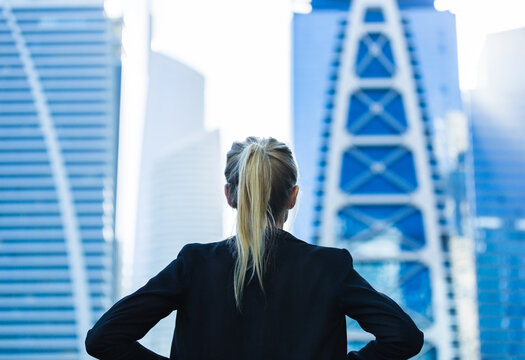 Business Career Challenge. Ambitious Businesswoman Overlooking The City Center High-rise Buildings With Hands On Hips. Back View.