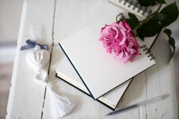 Pink rose flower on notebooks and plaster heart on a wooden stool