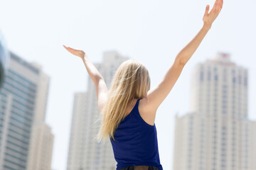 Positive young carefree woman celebrating success in the city with arms raised up during sunny summer day. 