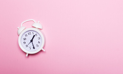 White alarm clock on pink background with copy space.