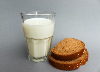  glass of milk with sliced dark ripe bread on grey background