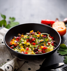 Healthy vegetarian salad with fresh vegetables and herbs in a black bowl  on a black table 