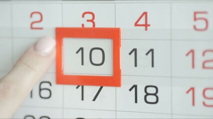 Woman's hand in office changes date at wall calendar. 10