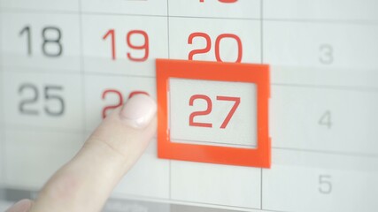 Woman's hand in office changes date at wall calendar. 27