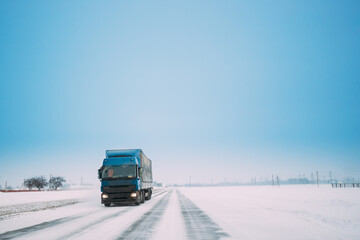 Blue Truck Or Tractor Unit, Prime Mover, Traction Unit In Motion On Winter Snowy Road, Freeway. Asphalt Motorway Highway During Snowfall. Business Transportation And Trucking Industry. Copy Space.