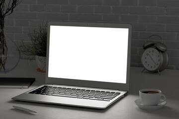 Workplace with glowing laptop screen at evening mock up.  White desk and brick wall. Side view. Clipping path round laptop screen. 3d illustration