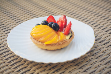 Custard fruit tart on white plate on 
wicker background