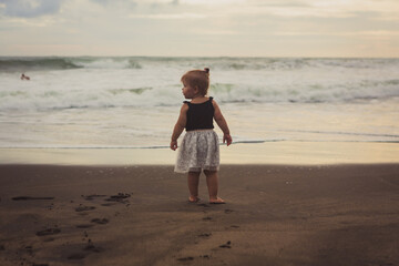 Happy little girl standing barefoot on the wet sand on the beach at sunset.