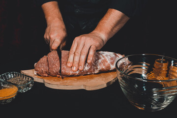 The chef of the restaurant in a dark uniform cuts the meat with a black kitchen knife. Preparation of pork marinated steak to order.