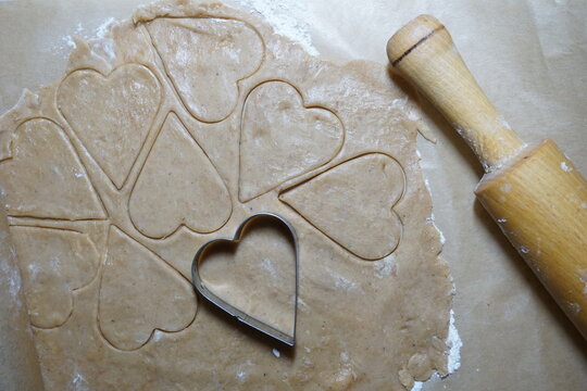 Heart shaped cookie cutters cutting out holiday cookies.