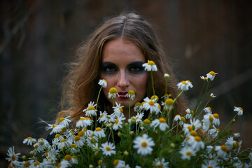 witch girl with a bouquet of daisies in a dark pine forest