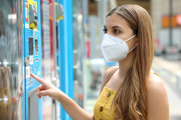 Portrait of young woman with protective mask KN95 FFP2 choosing a snack or drink at vending machine in train station. Vending machine with girl. - obrazy, fototapety, plakaty