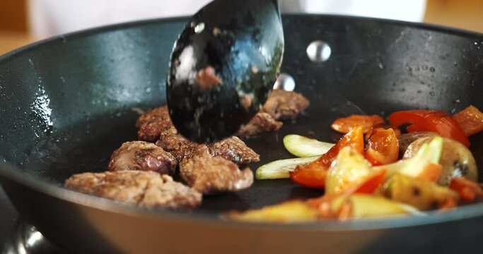 Meat and vegetables cooking frying in pan. Chef mixing food with spoon.