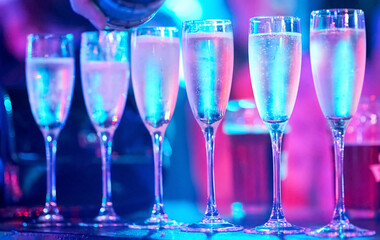 A row of full champagne glasses illuminated with pink and blue lights