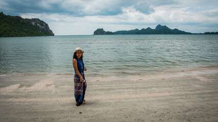 woman in white fedora hat and sarong standing on the beach with islands in the background