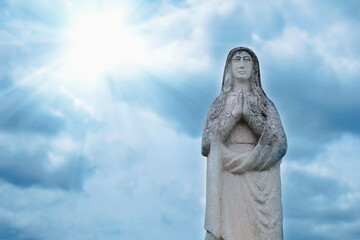 Fototapeta na wymiar Ancient stone statue of Virgin Mary against blue sky.
