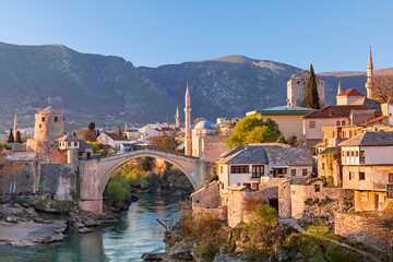 Skyline of Mostar with the Mostar Bridge, houses and minarets, at the sunset in Bosnia and Herzegovina - obrazy, fototapety, plakaty