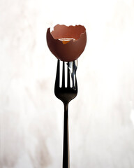 Creative advertising photo of an egg on a fork. Matte black fork on a light background.Raw egg in a shell with the protein running down. Copy space