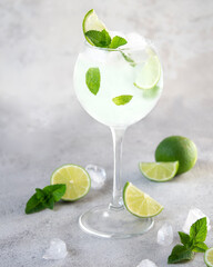Fototapeta premium Refreshing lemonade with lime and mint slices in a glass steamed glass on a gray background. Mojito ads for the catalog. Of half a lime, ice. Food styling of a summer drink. Copy space