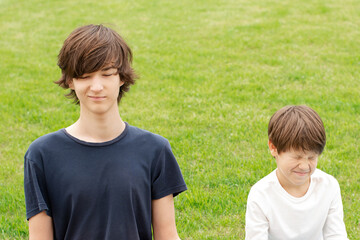 teenager and boy squint with closed eyes and a grin on his face. Green grass lawn. Copy space