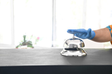 Male hand in protective gloves ringing hotel bell with copy space for your text    
