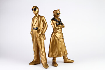 Fototapeta na wymiar Golden plaster figures of man and woman. Vintage style. The man in a classic suit and sunglasses, the woman in a skirt and shirt with sunglasses and folded arms. White background