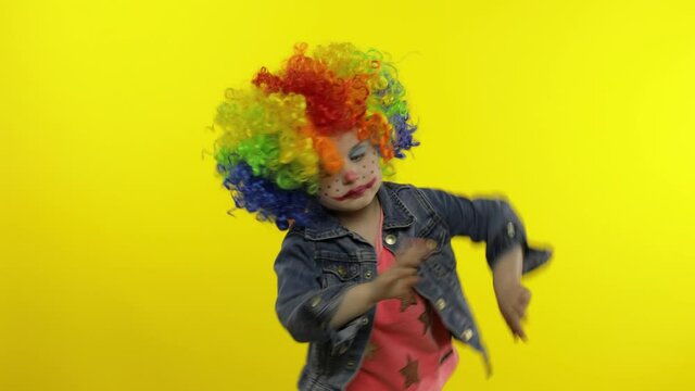 Little child girl clown in colorful wig making silly faces. Having fun, smiling, dancing. Halloween