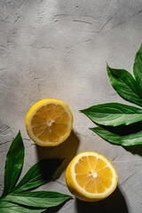 Two lemon slices, tropical citrus fruits with green leaves on grey concrete background, top view copy space