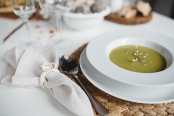 green soup in a white plate on a white table with spoon and serviette