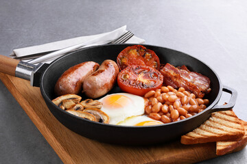 English breakfast in a pan on a gray background. Fried sausages, bacon, eggs, mushrooms, tomatoes and beans.